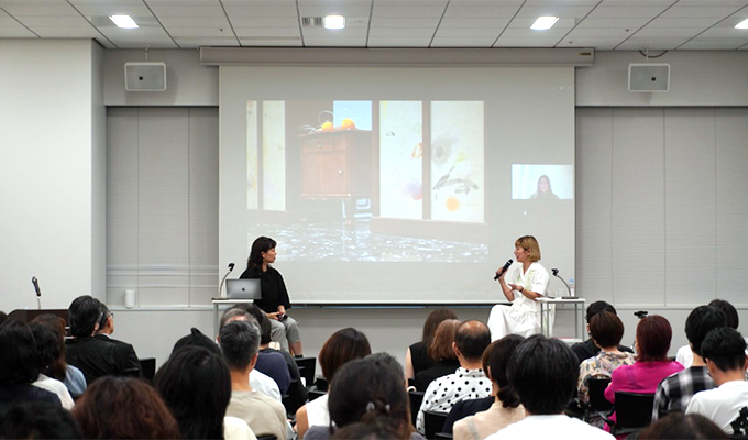 Two people giving a report from the back of the venue, looking through the projector screen over the audience's shoulders