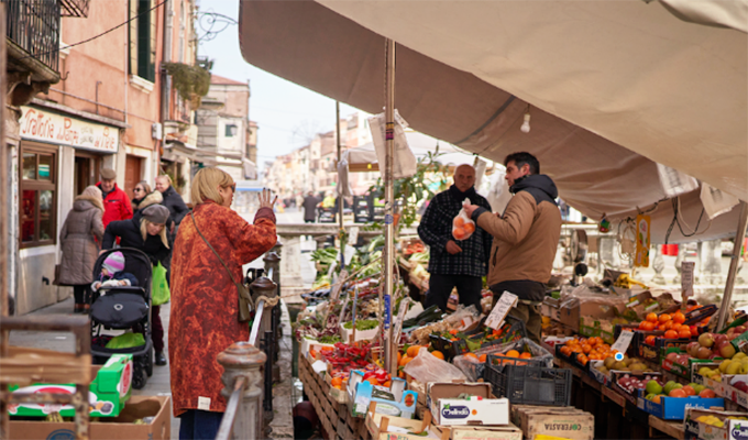 A man buying fruit from two salespeople in front of a fruit stall in a market