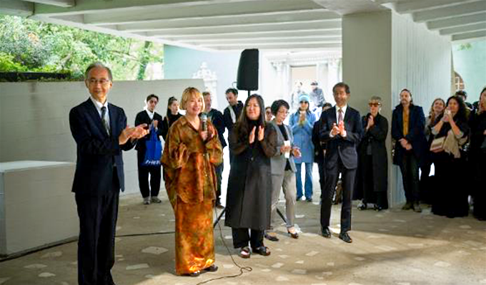 Two people giving speeches on the outside of the building, surrounded by people clapping